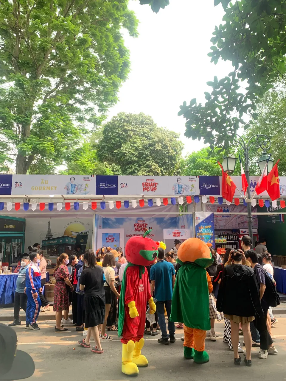 Hai mascot Fruit Me Up đi giữa dòng khách trước dãy gian hàng lễ hội