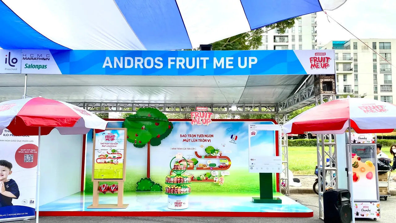 Booth Andros Fruit Me Up dưới mái che tại khu sự kiện của giải HCMC Marathon, với cây táo, khu trưng bày và hai dù hai bên