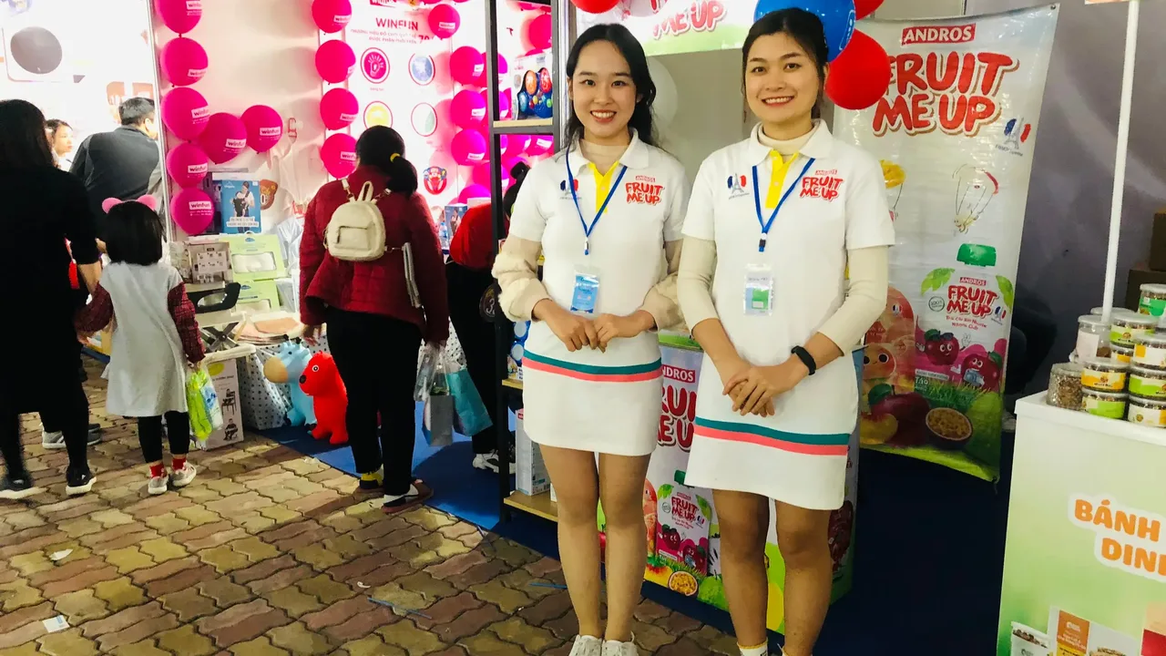 Hai PG Fruit Me Up đứng tại gian hàng trong sự kiện mẹ và bé của Kids Plaza ở Sân vận động Quần Ngựa