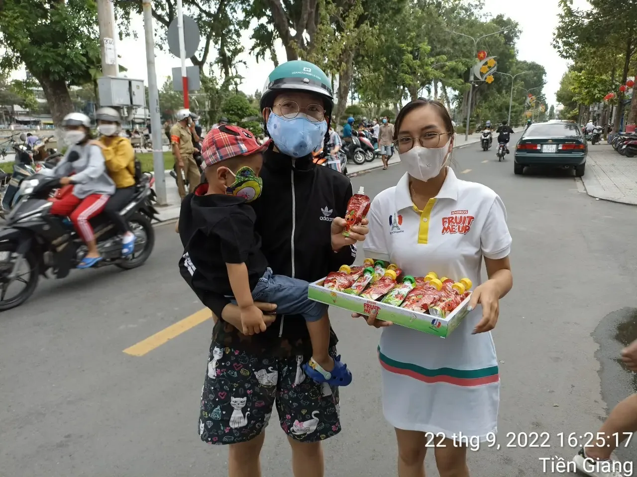 PG Fruit Me Up cầm khay sản phẩm đứng cùng một phụ huynh đón con tan học ở Tiền Giang