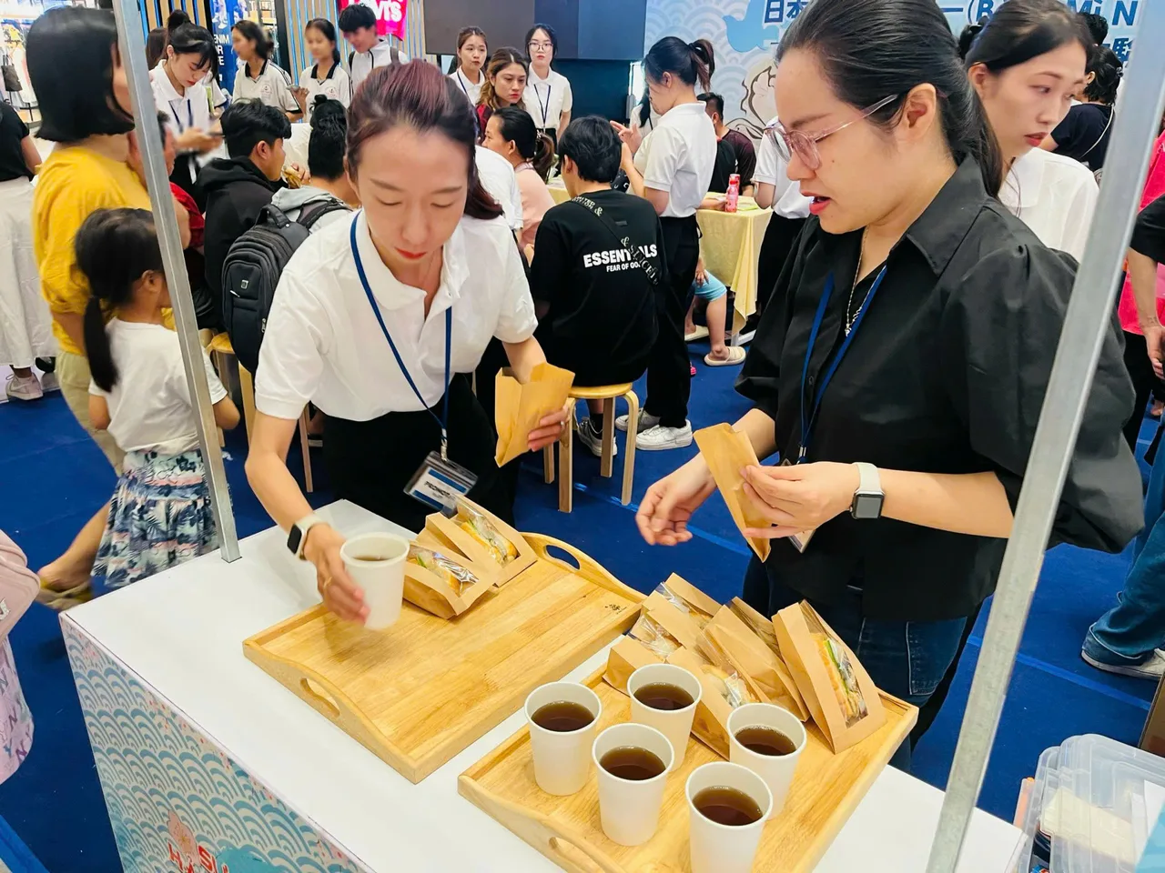 PG chuẩn bị khay bánh mì và trà trên booth chế biến trong lúc khách đứng chờ