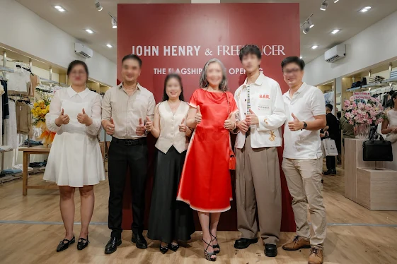 Khách mời chụp hình trước backdrop đỏ đô mang tên John Henry & Freelancer bên trong cửa hàng