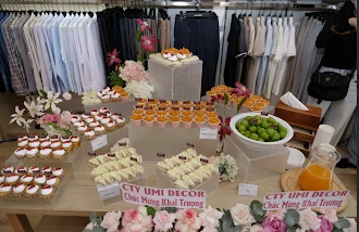 Bàn tiệc nhẹ bày bánh, nho và nước ép cam giữa các kệ quần áo trong cửa hàng