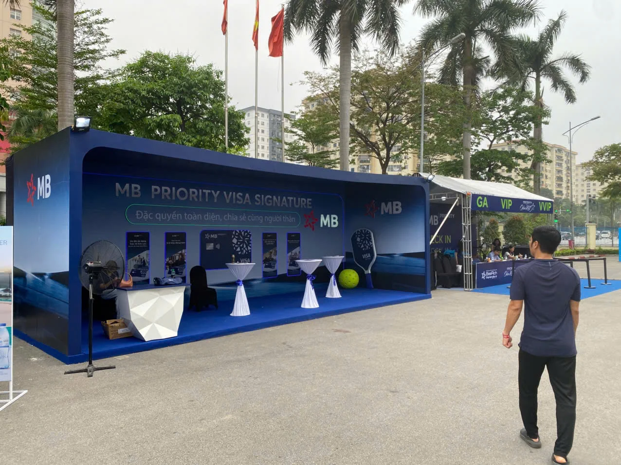Khu tư vấn tông xanh đậm mang tên thẻ, bàn cocktail trắng trên sân bê tông lúc chưa đông khách