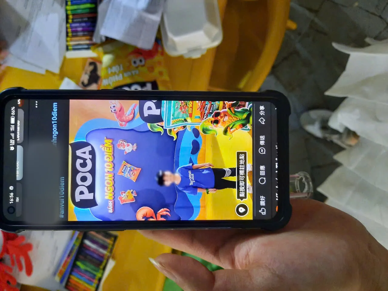 Khách đưa bài check-in Facebook chụp tại vách Poca Playground cho PG xem, phía sau là bàn bút sáp của góc tô màu
